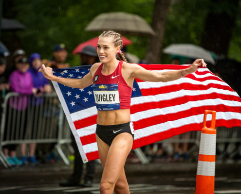 Colleen Quigley national champion. Colleen is smiling holding the american flag around her shoulders. it's raining in New York City.