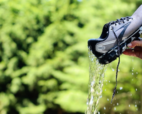 wet running shoes. water is being poured out of them. running shoes are Brooks brand. Background is green trees.