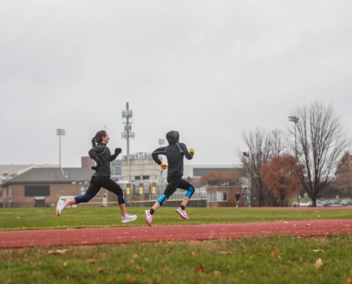 two females runners running fast on the track doing intervals in the rain.