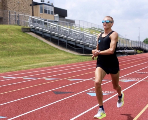 Man splitting his watch to get his pace while running a workout at the track. He is a blond marathon runner wearing sunglasses.