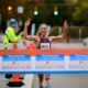 molly bookmyer crossing the finish line of a race breaking the tape. she is smiling and raising her hands.